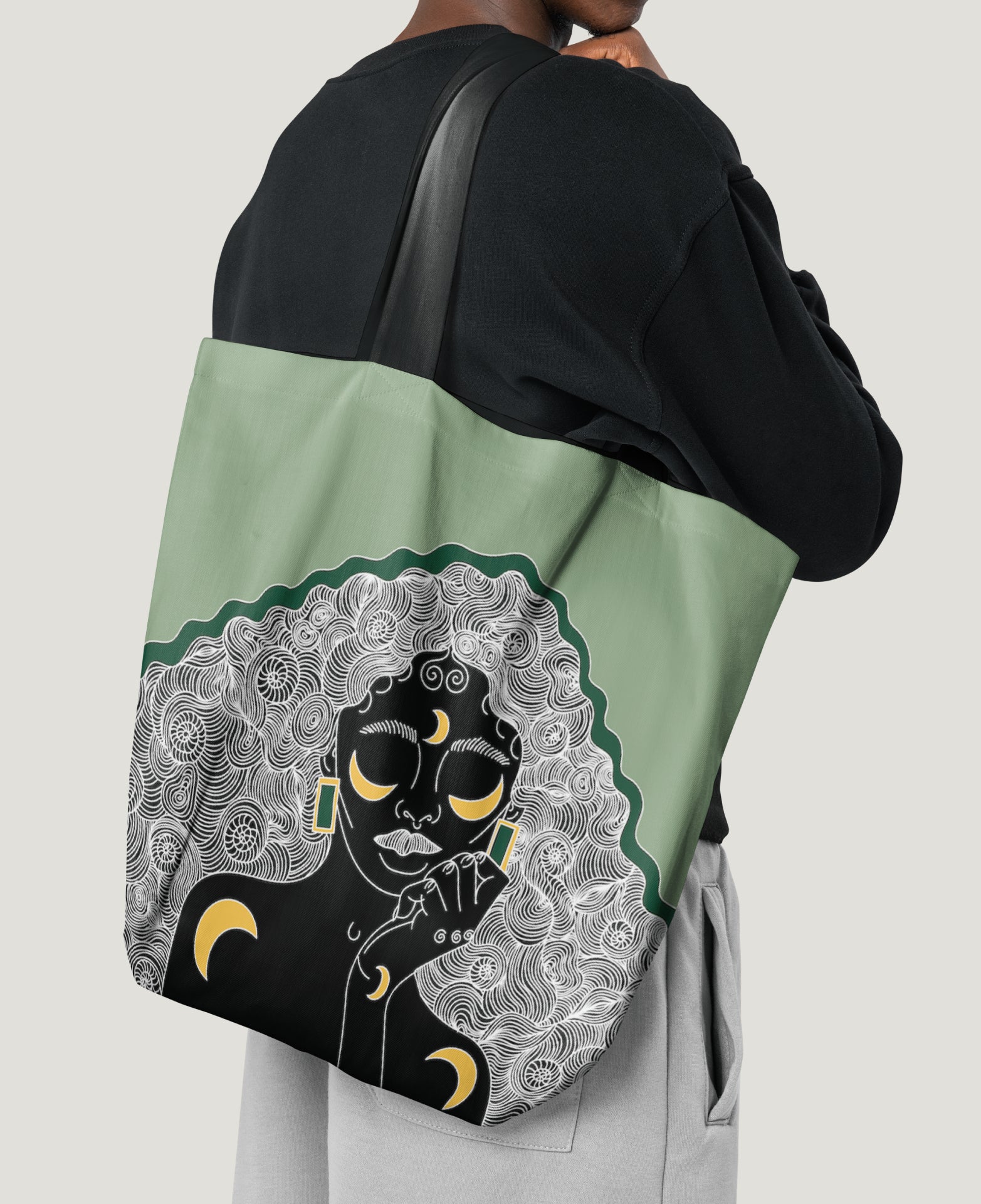 A person carrying a green tote bag with an illustration of a person's head and moon and stars on it.